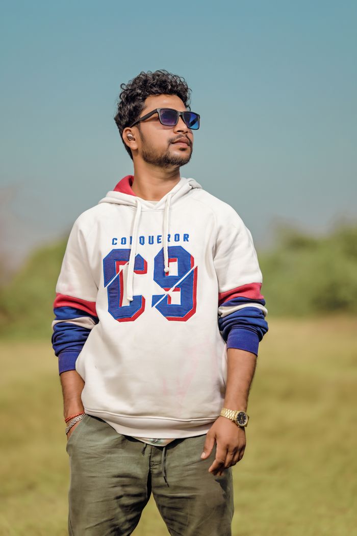 Young man in hoodie and sunglasses standing confidently in a field.